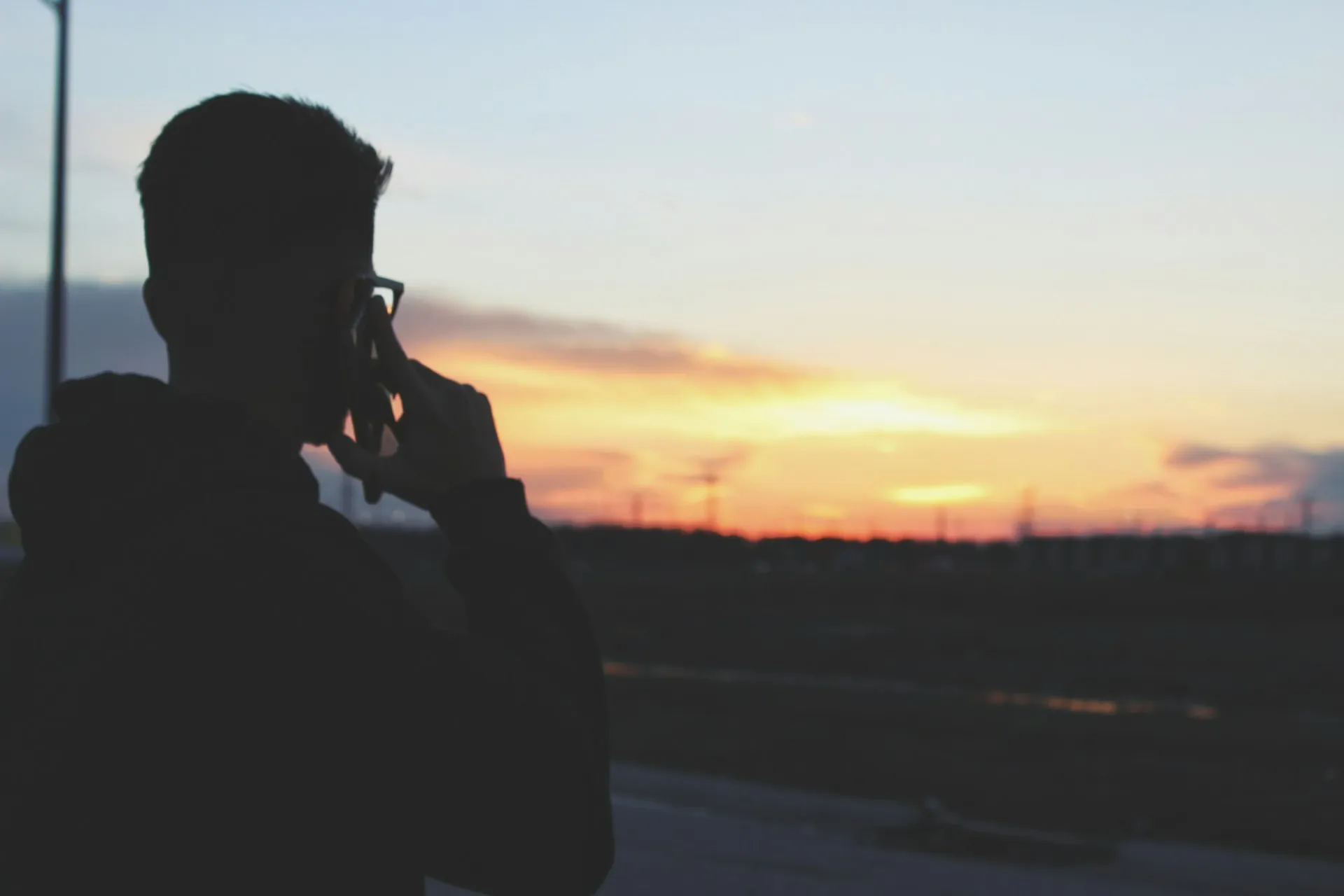 A man on a cell phone looking at the sunset