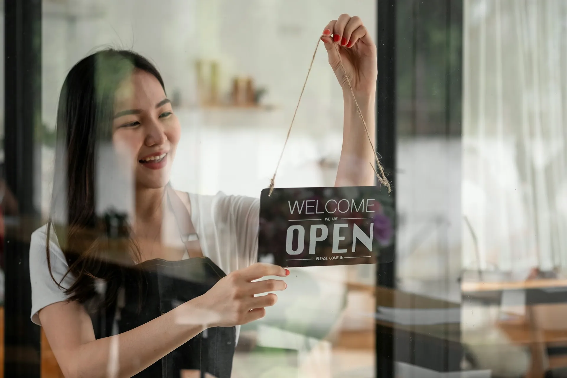 A woman smiles as she turns a closed sign to an open sign on the door of her business