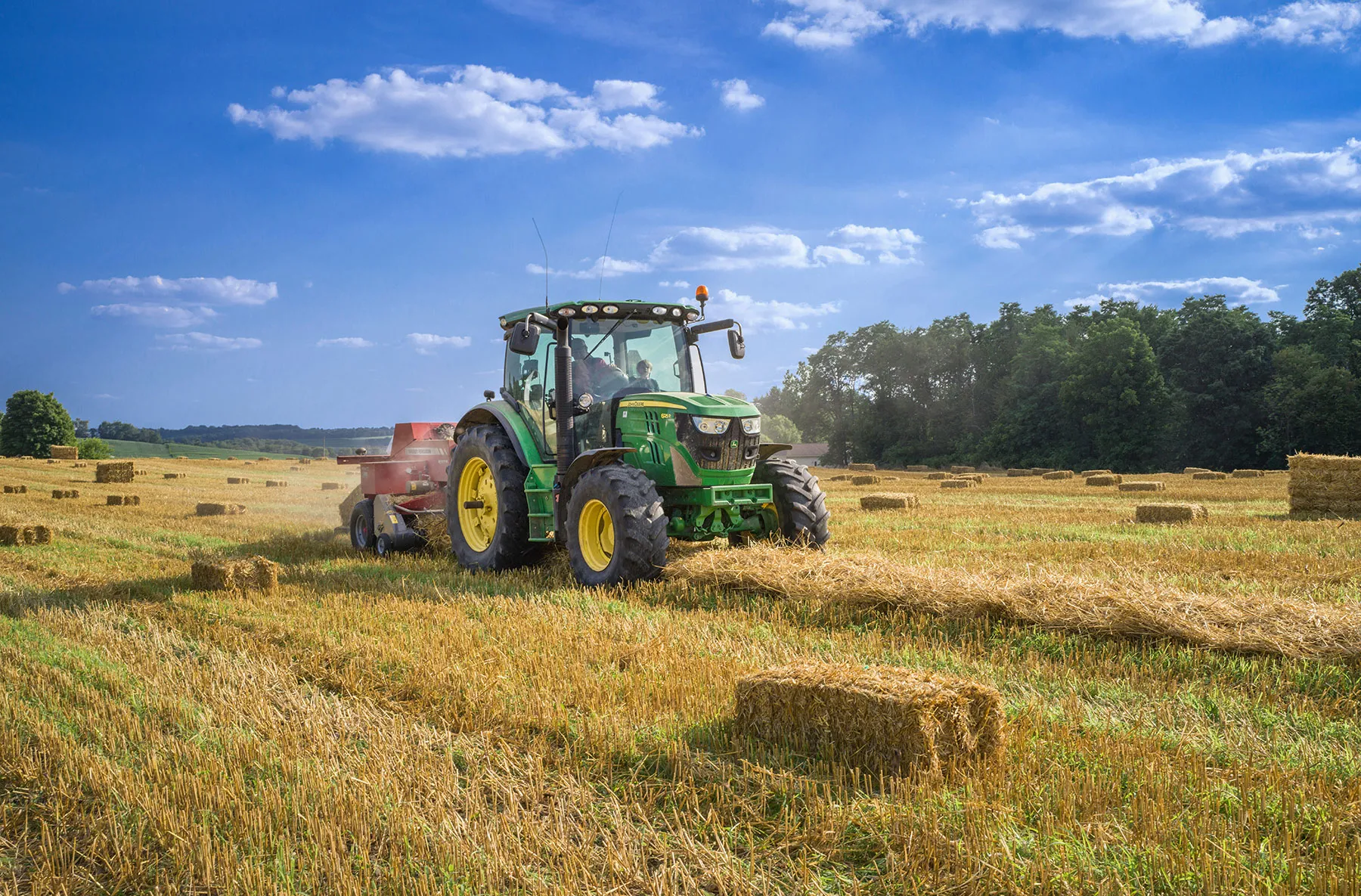 A tractor baling hay in a field under blue skies