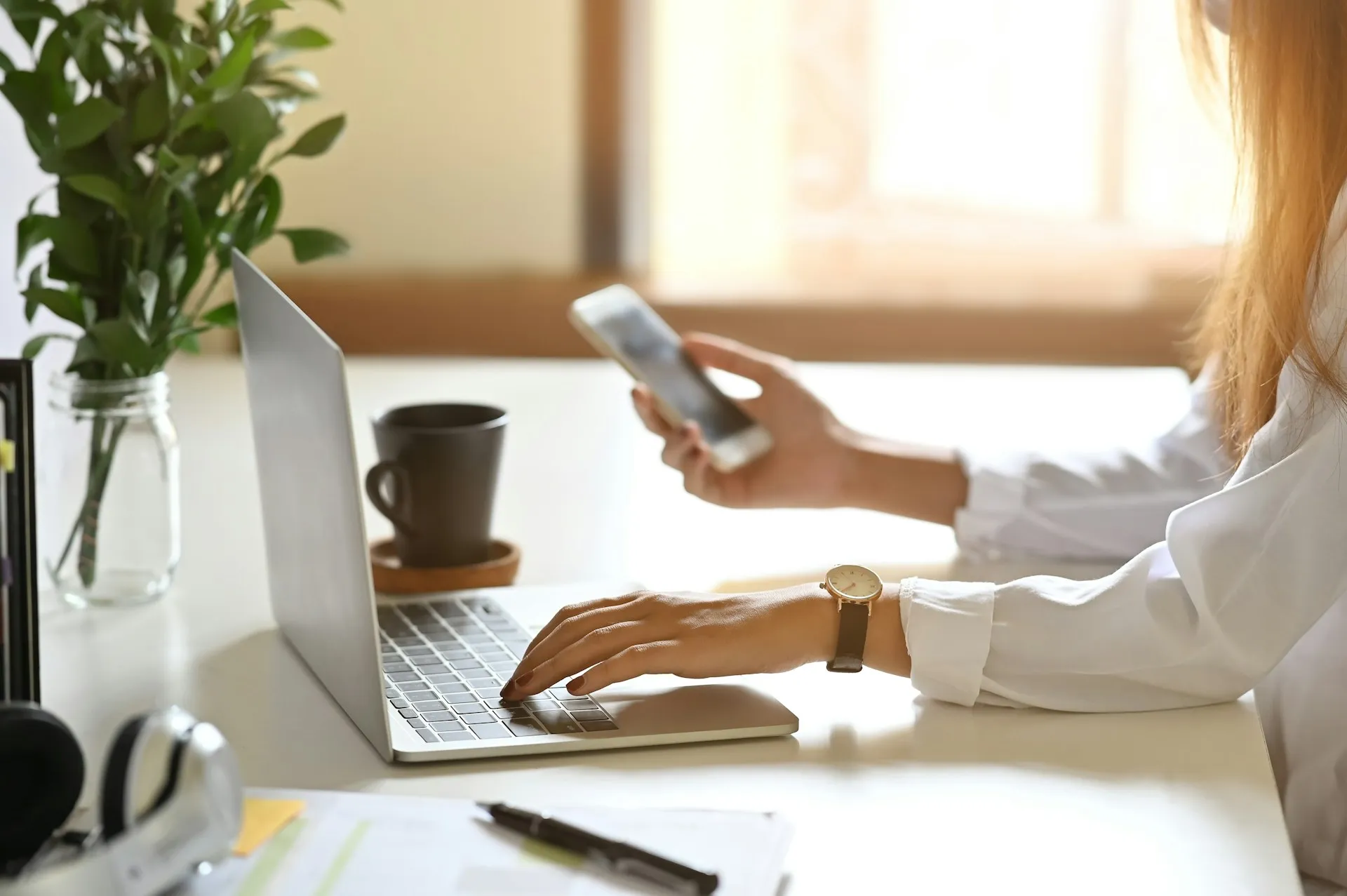 A woman typing on a laptop with one hand and holding her phone in the other