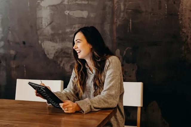 A laughing woman holding a notebook at a conference table